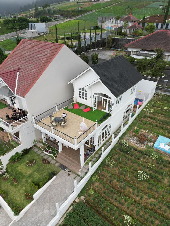 Aerial shot of modern white house with lush garden and terrace seating.